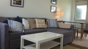 Una sala de estar con un sofá gris, una mesa de centro blanca y una zona de comedor con mesa y sillas.