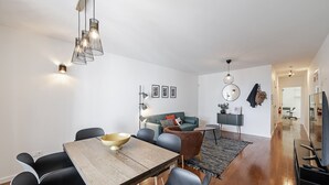 Ein modernes Wohnzimmer mit einem Holzes Esstisch, schwarzen Stühlen, einer Couch und einem Fernseher.