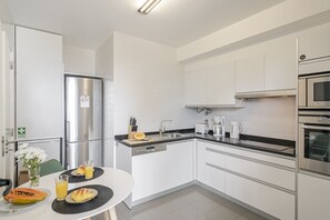A modern kitchen with white cabinetry, stainless steel appliances, and a dining area with a table set for breakfast.