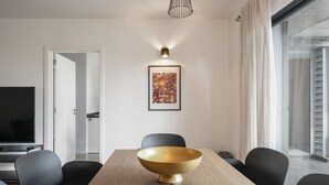 Ein moderner Essbereich mit einem Holztisch, schwarzen Stühlen, einer großen goldfarbenen Schale als Mittelpunkt, einem gerahmten Kunstwerk über dem Tisch und einem Fernseher im Hintergrund.
