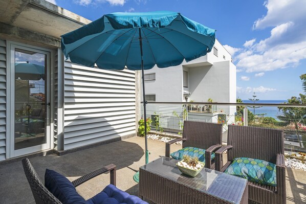 A balcony with wicker furniture, a table, and a blue umbrella.