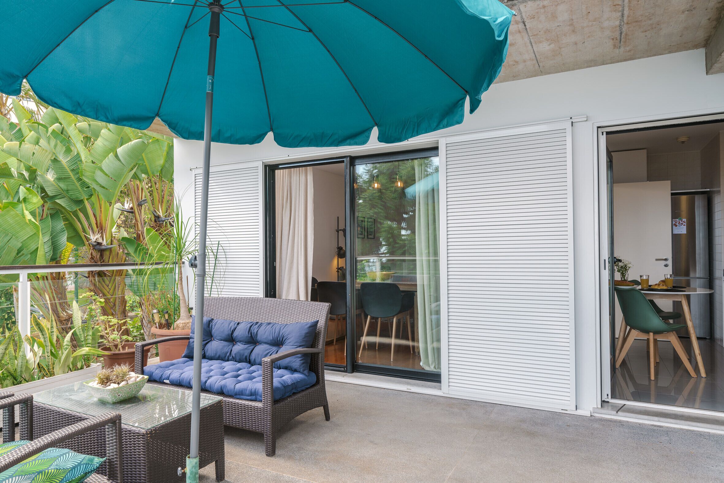 Un balcon agrémenté d’un parasol bleu, de meubles en osier et de plantes en pot.