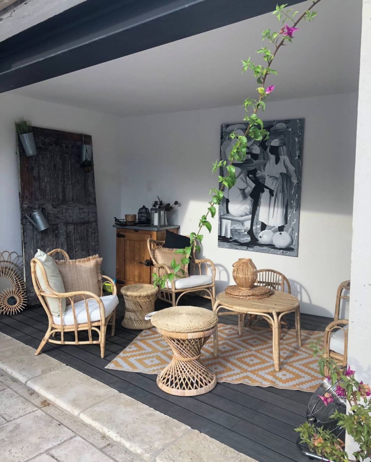 Un espacio al aire libre con mobiliario de mimbre, una mesa trenzada y un cuadro grande en blanco y negro en la pared.