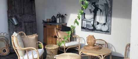 Un espacio al aire libre con mobiliario de mimbre, una mesa trenzada y un cuadro grande en blanco y negro en la pared.