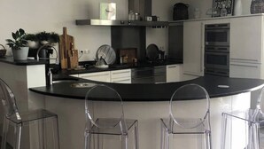 A modern kitchen with a curved island, clear plastic chairs, and a stainless steel range hood. - Air-conditioned town house with heated swimming pool (Arles)