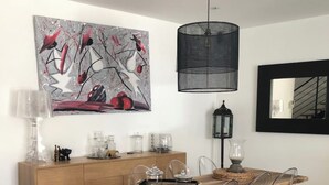A modern dining area with a wooden table, clear chairs, a black pendant light, a wooden cabinet, and a large abstract painting on the wall. - Air-conditioned town house with heated swimming pool (Arles)