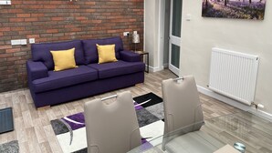 Un salon moderne avec un canapé violet, une table en verre et un mur en briques.
