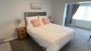 Une chambre à coucher avec un grand lit, une table de chevet, une lampe, un radiateur et une fenêtre avec des rideaux.