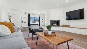 Een moderne woonkamer met een bank, een houten salontafel en een televisie die aan een witte bakstenen muur is bevestigd.