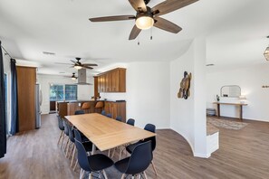 A modern kitchen with wooden cabinets, a dining area with a wooden table and black chairs, and ceiling fans.