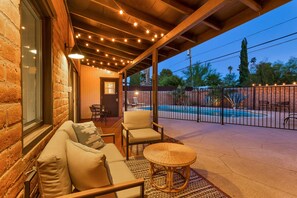 A covered outdoor seating area with a pool, a brick wall, and string lights.
