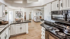 A spacious kitchen with white cabinetry, a black stove, and a large island. There is a dining area with a sofa and a coffee table.