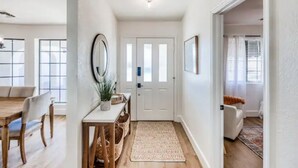 A hallway with a wooden floor, a white door, and a dining area with a table and chairs.