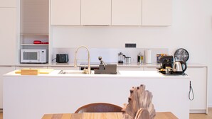 A modern kitchen with white cabinetry, a central island with a sink, a microwave, a coffee maker, and a kettle. - R213 - Exquisite City Sanctuary, Brussels (Saint-Josse-ten-Noode)