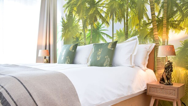 A bedroom with a bed, pillows, a nightstand, a lamp, and a wall mural of palm trees. - R213 - Exquisite City Sanctuary, Brussels (Saint-Josse-ten-Noode)