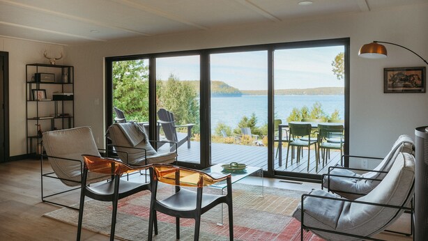 Ein modernes Wohnzimmer mit einem großen Schiebeglasfenster, das auf eine Terrasse mit Seeblick und Bergblick führt.