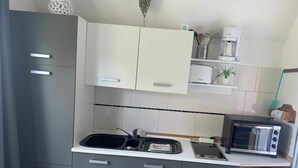 Cocina compacta con gabinetes grises, encimera blanca, horno empotrado, cafetera y tostadora.