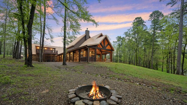 Une cabane avec un foyer en pierre à l’avant, entourée d’arbres.