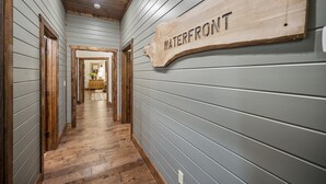 Un couloir avec un plancher en bois, des murs gris et une enseigne en bois sur laquelle on peut lire « AU BORD DE L’EAU ».