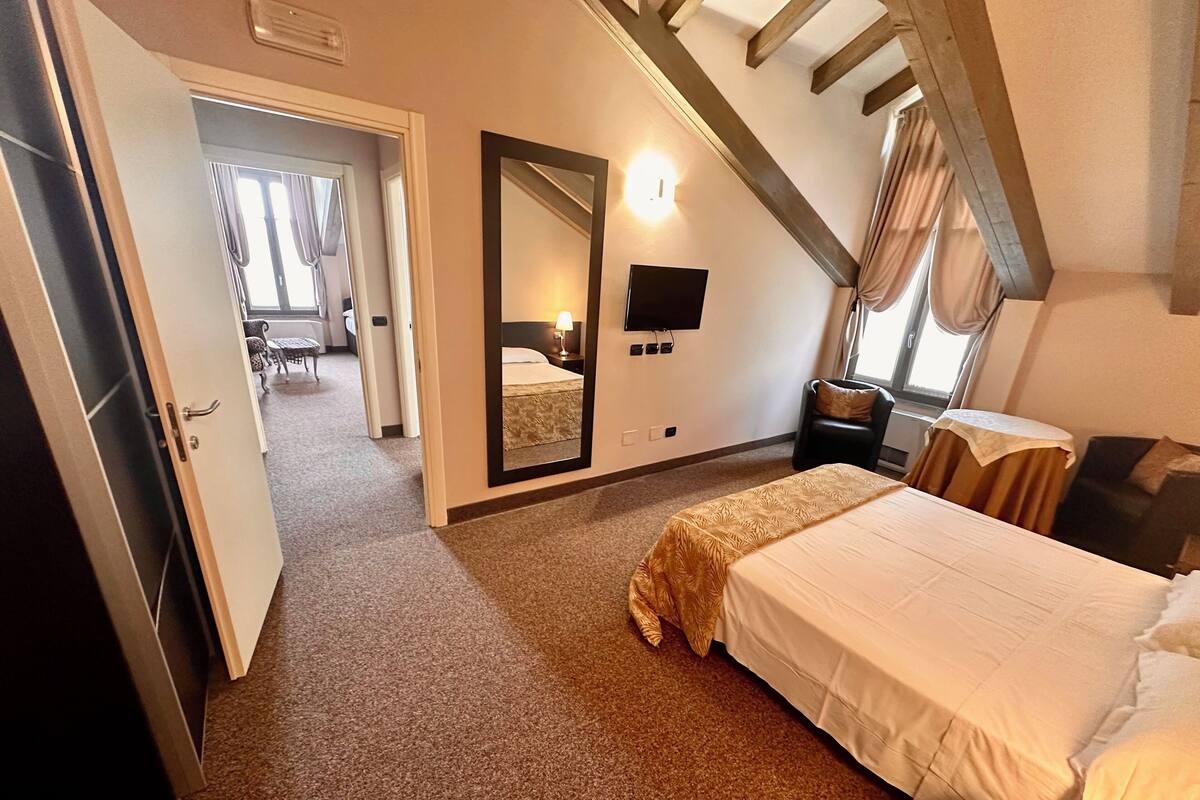A hotel room with a bed, a mirror, a TV, and a small table.
