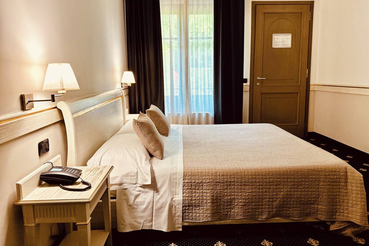 A hotel room with a bed, bedside lamps, a telephone, and a door.