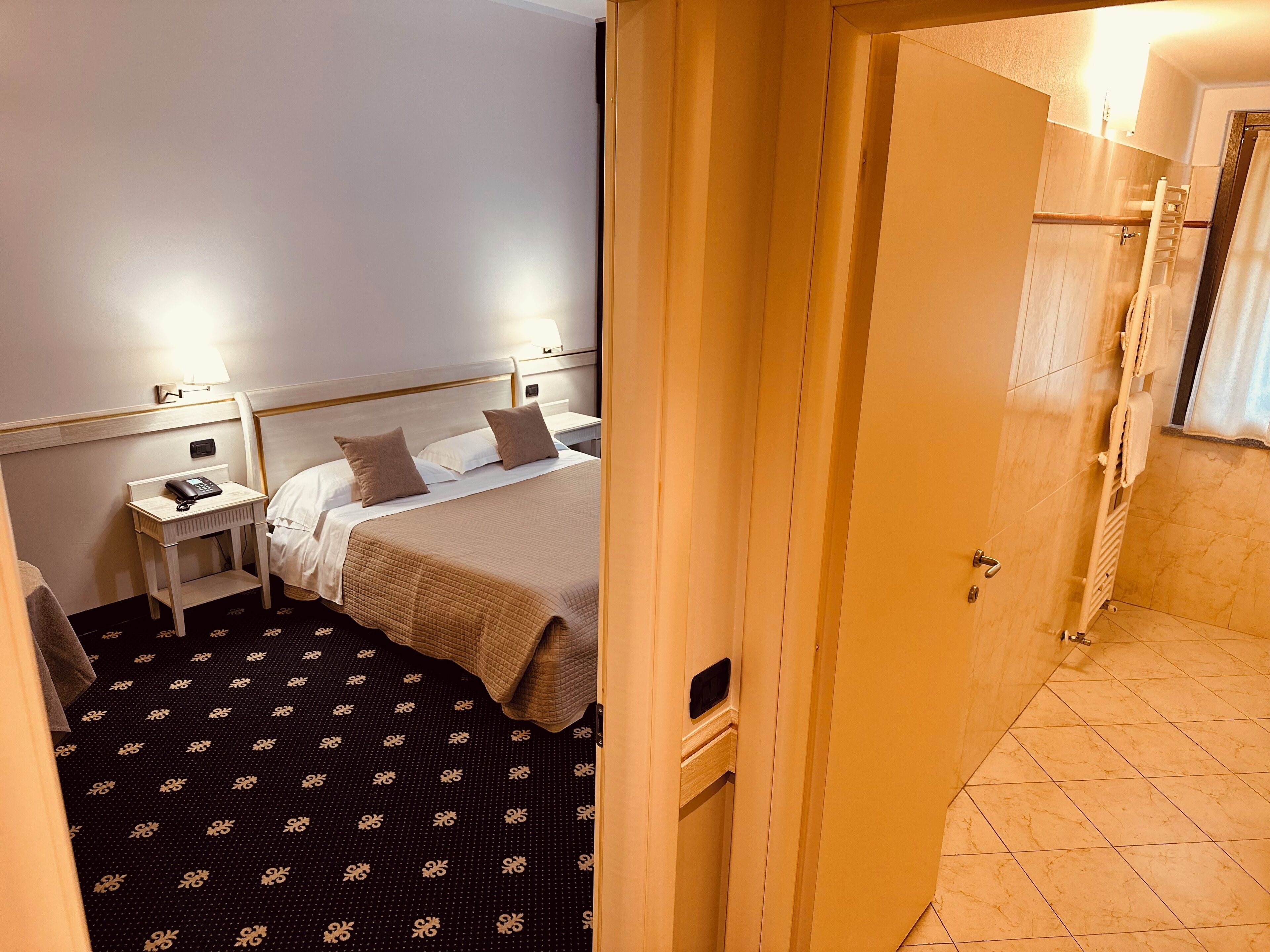 A hotel room with a bed, bedside table, lamp, and a bathroom with a shower and towel rack.
