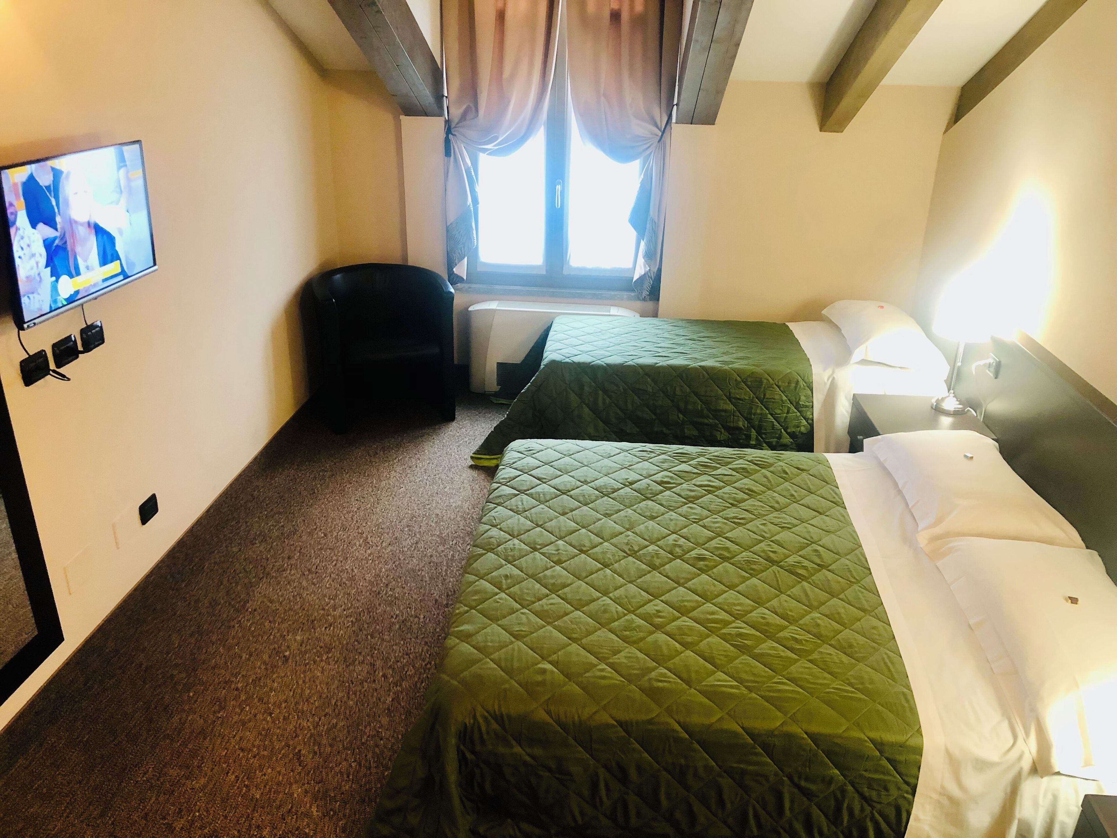 Een hotelkamer met twee bedden, een televisie, een raam met gordijnen en een kleine stoel.