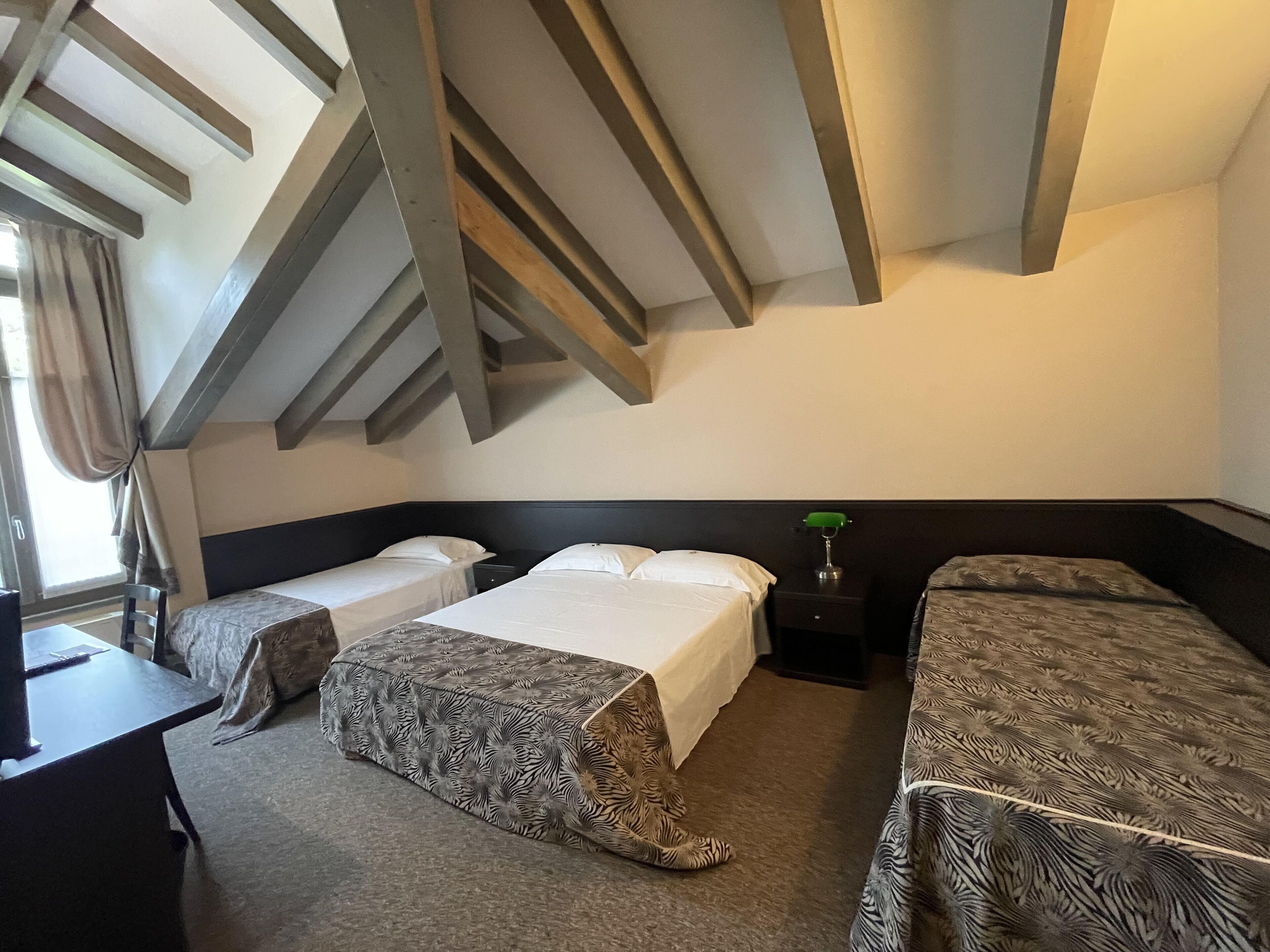 A hotel room with two beds, a desk, and a window with curtains.