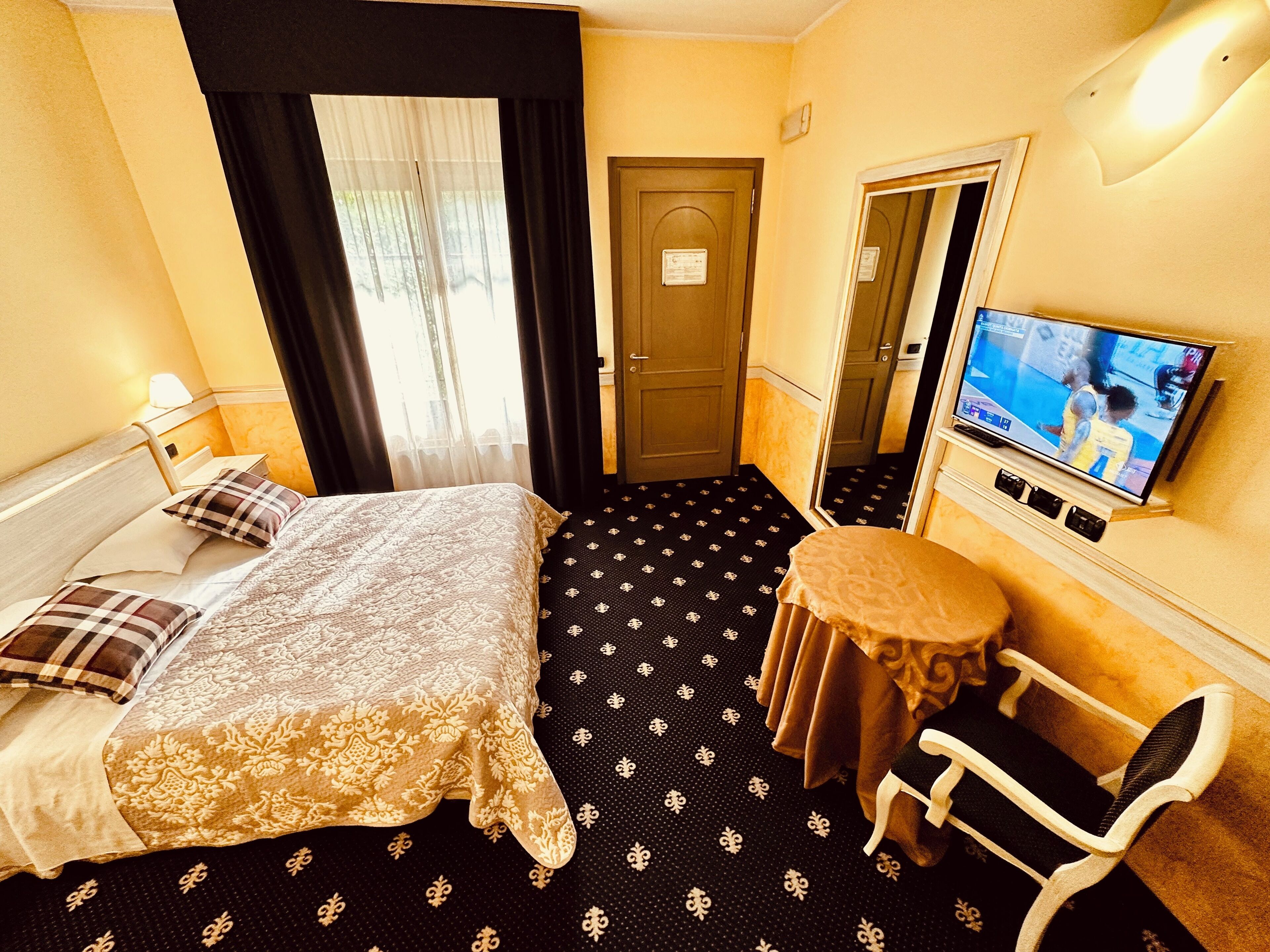Ein Hotelzimmer mit einem Bett, einem kleinen runden Tisch, einem Sessel, einem Fernseher und einer Tür.