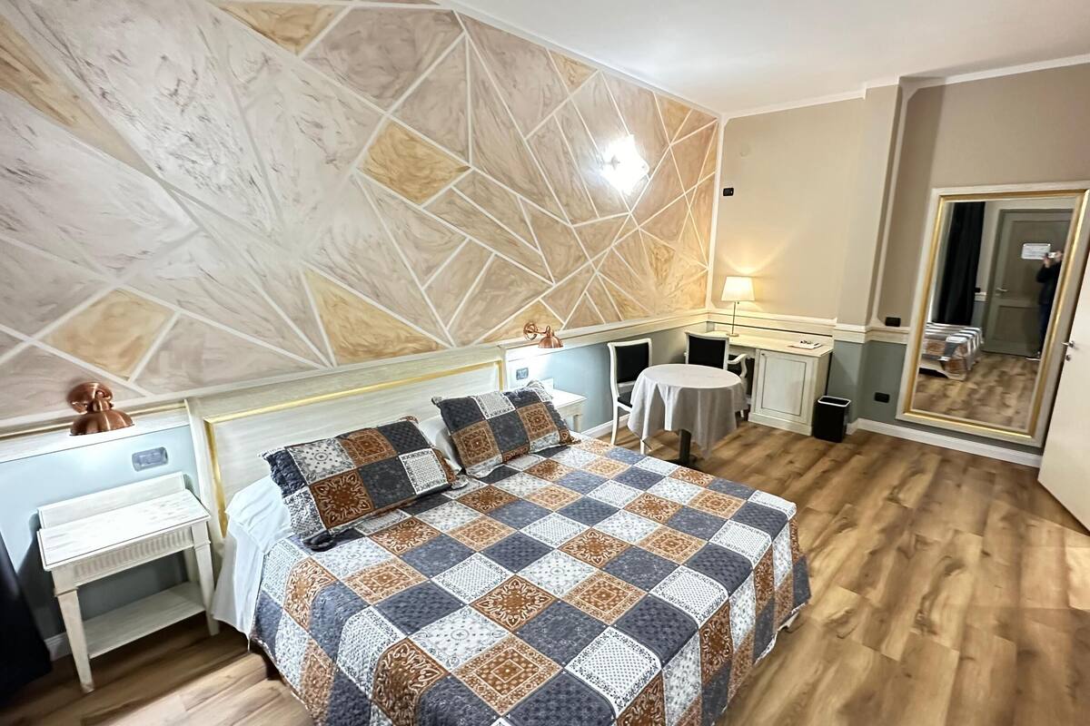 A bedroom with a large bed, a desk, a chair, and a small table.