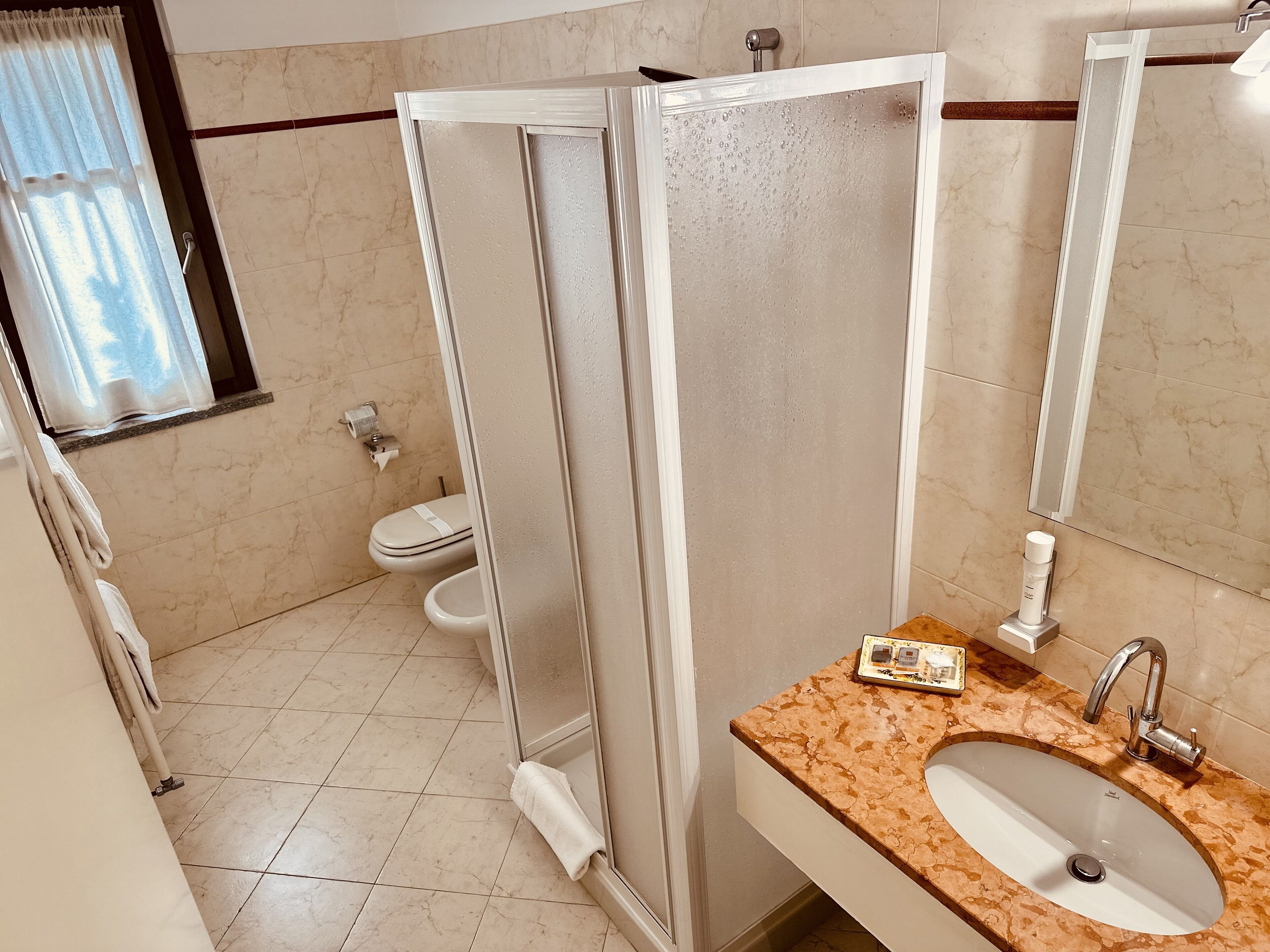 A bathroom with a shower enclosure, toilet, sink, and a towel rack.