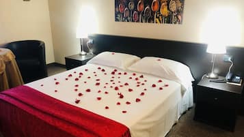 A hotel room with a neatly made bed, two bedside tables with lamps, a chair, and a painting on the wall.