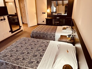 A hotel room with two beds, a desk, a chair, a mirror, and a lamp. - Hotel Malpensa Inn (Lonate Pozzolo)