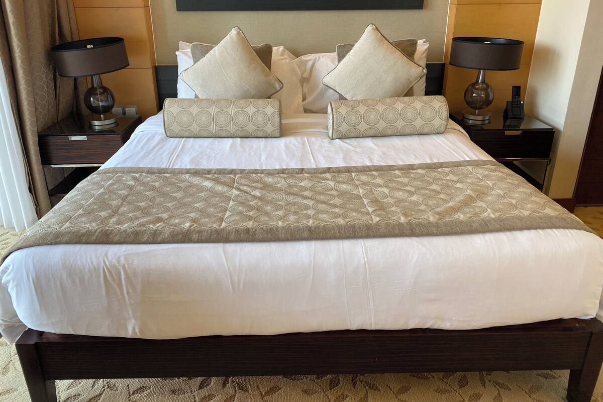 A neatly made bed with a patterned throw, two bedside tables with lamps, and a painting on the wall.