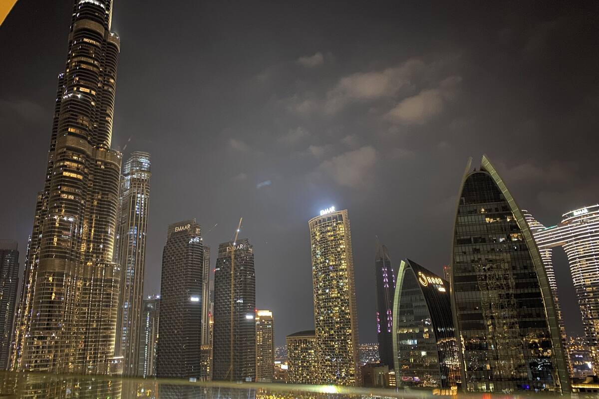 A nighttime cityscape with modern skyscrapers, including a prominent curved building and several high-rise structures with illuminated windows.