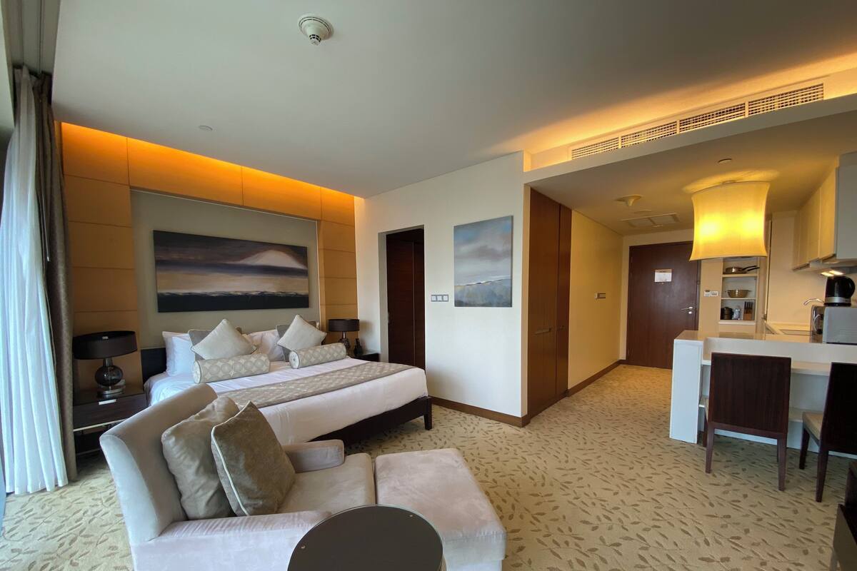 A hotel room with a bed, a sofa, a small table, a desk, and a kitchenette.
