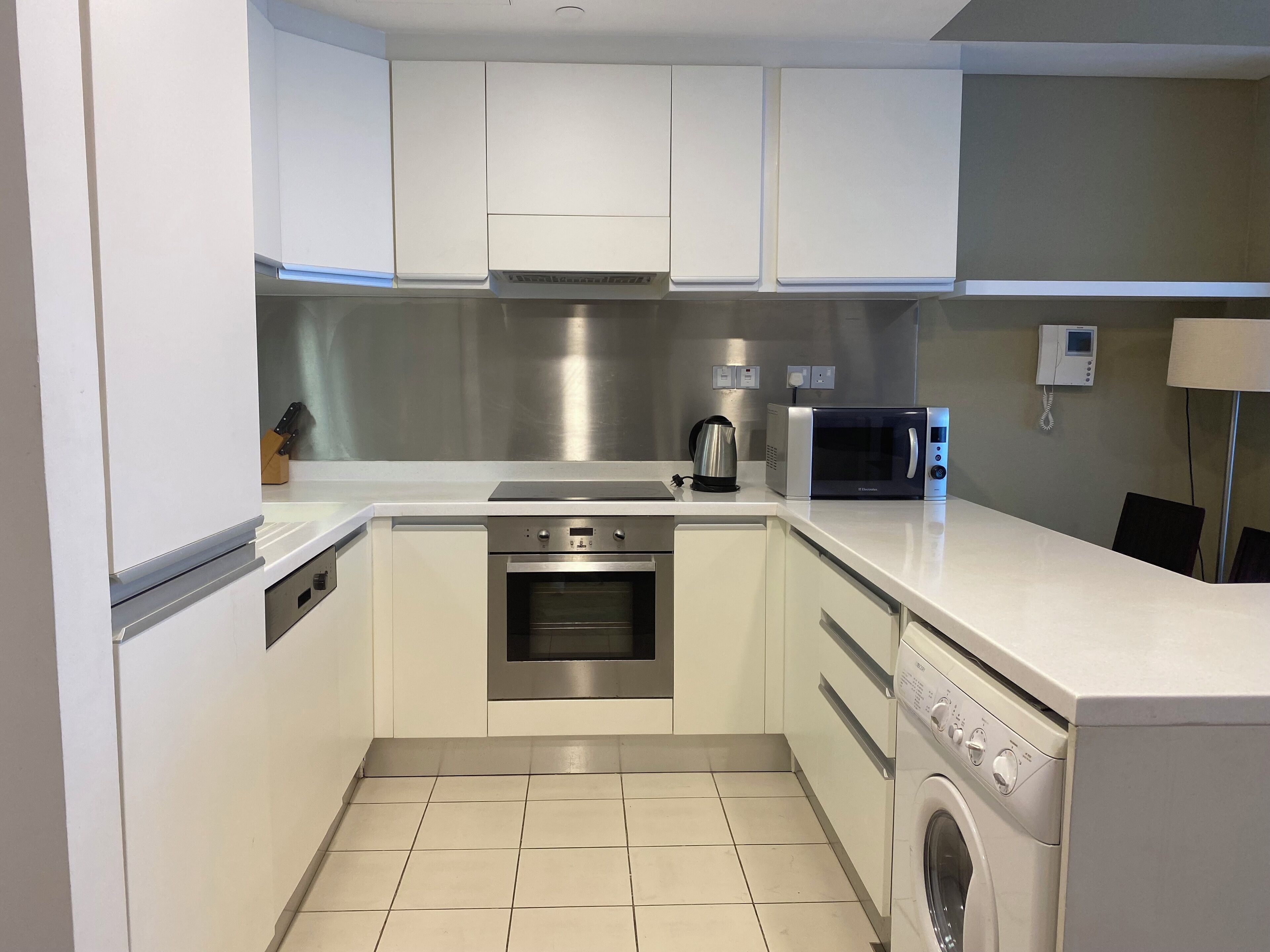 A modern kitchen with white cabinets, stainless steel appliances, a microwave, a coffee maker, and a washing machine.