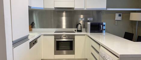 A modern kitchen with white cabinets, stainless steel appliances, a microwave, a coffee maker, and a washing machine.