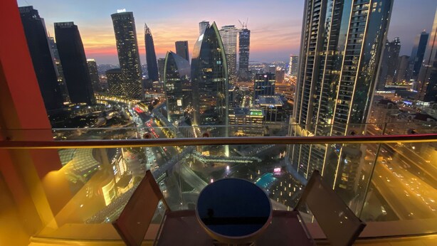 Vue sur la ville depuis un immeuble de grande hauteur à l’architecture moderne, avec un espace repas comprenant une table ronde et des chaises.