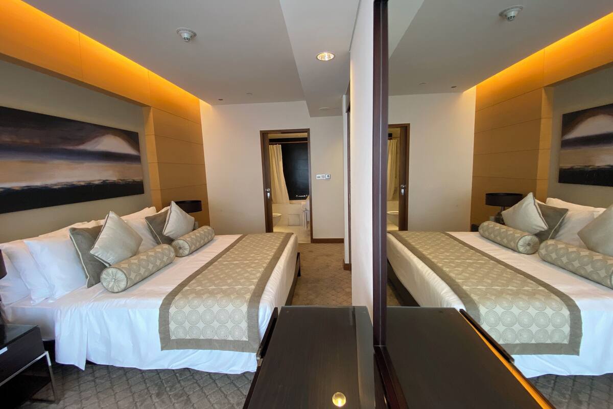 A hotel room with two beds, a large mirror, and a view of the bathroom.