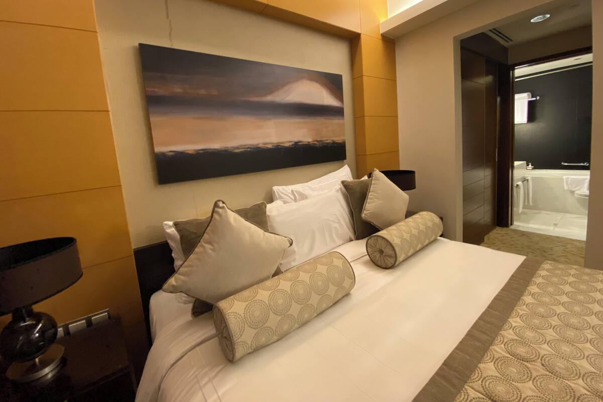 A hotel room with a large bed, a painting on the wall, and a bathroom visible through an open door.
