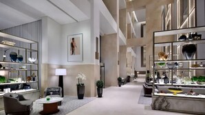 Un hall d’hôtel spacieux avec un espace salon central, un comptoir d’accueil et des étagères où sont exposés des objets décoratifs.