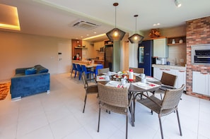 A modern kitchen with a built-in oven and a dining area with wicker chairs and a round table. - VG Sun Pé na Areia Luxuoso Térreo Gourmet 8 pessoas By DM Apartments (Caucaia)