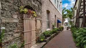 A narrow brick pathway flanked by buildings with stone walls and wooden shutters.