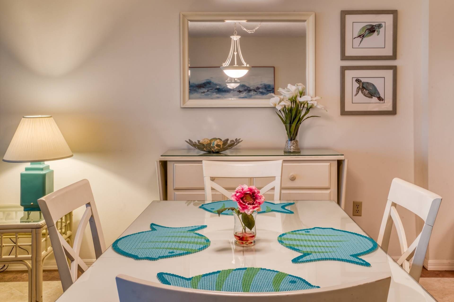 A dining area with a white table, chairs, a vase with flowers, and framed artwork on the wall.