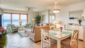 A spacious living area with a large window overlooking the ocean, a ceiling fan, and a dining table with chairs. - Sand Dollar #205 (St. Augustine)