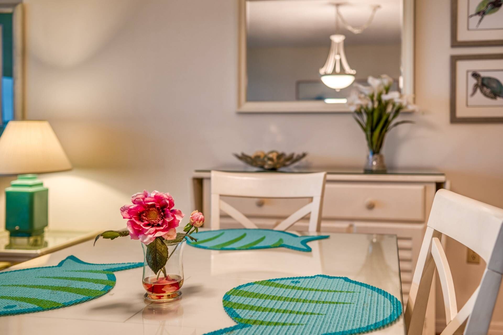 A dining area with a table set for two, a vase with flowers, and a decorative bowl on the side table.