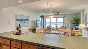 A modern kitchen with a green countertop, wooden cabinets, and a dining area with a view of the ocean. - Sand Dollar #205 (St. Augustine)