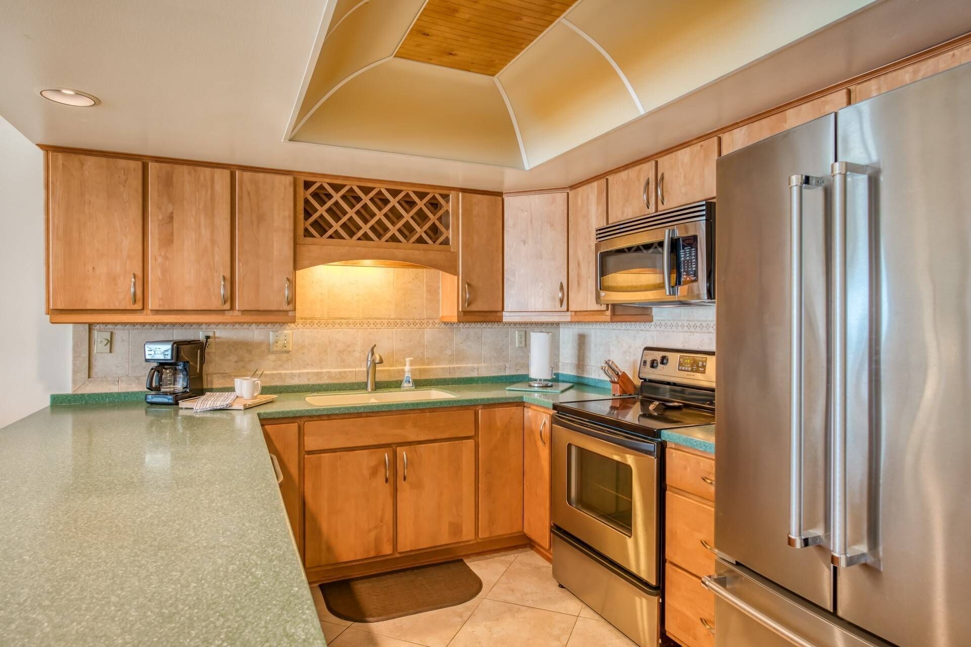 A modern kitchen with wooden cabinets, a stainless steel refrigerator, a microwave, and an oven.