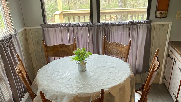A round dining table with a white tablecloth, surrounded by wooden chairs. - A Cozy Camp Located 5 Minutes from State Gamelands and a Stocked Trout Stream… (Homer City)